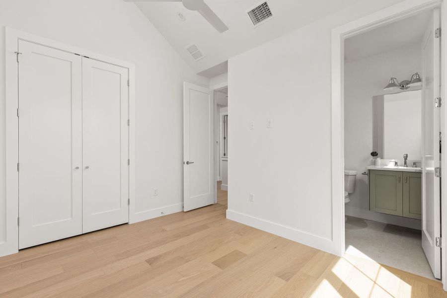 Unfurnished bedroom with connected bathroom, light wood-type flooring, and vaulted ceiling