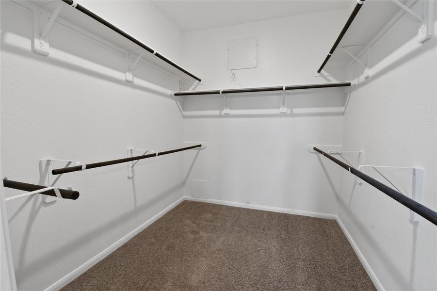 This photo shows a spacious walk-in closet with multiple hanging rods and carpeted flooring, offering ample storage. This photo shows a spacious walk-in closet with multiple hanging rods and carpeted flooring, offering ample storage.