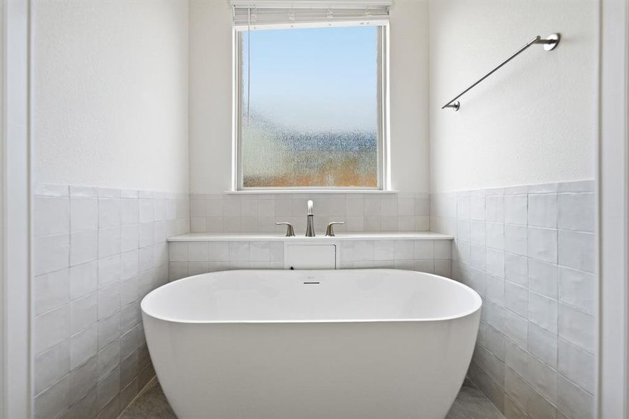 Freestanding soaking tub with polished chrome fixtures, surrounded by white square wall tiles and a built-in ledge