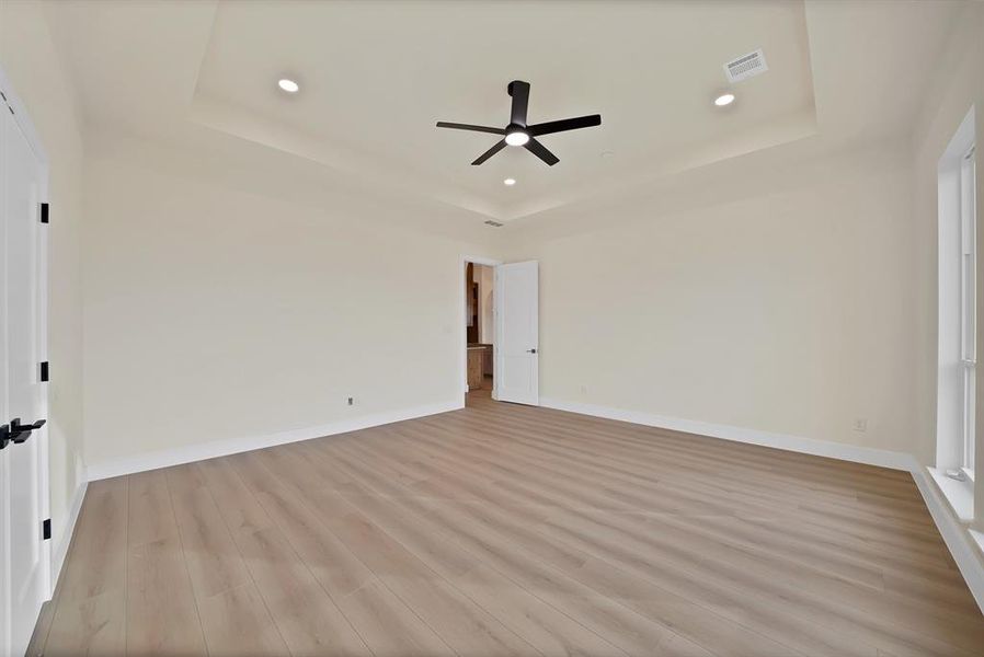 Unfurnished bedroom with a tray ceiling, light wood-style floors, a ceiling fan, and recessed lighting Unfurnished bedroom with a tray ceiling, light wood-style floors, a ceiling fan, and recessed lighting