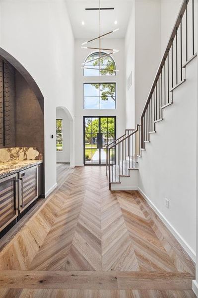 Interior view of the grand entryway with soaring ceilings and Visual Comfort chandelier. The large windows and double front doors allow ample natural light to fill the space, creating a bright, airy feel.