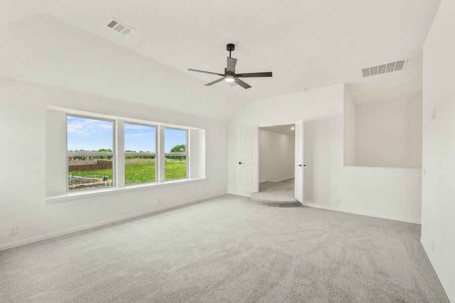 Spacious empty bedroom with gray carpet, ceiling fan, and large windows overlooking a green yard Spacious empty bedroom with gray carpet, ceiling fan, and large windows overlooking a green yard