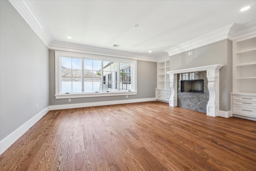 This view of the primary bedroom with hardwood floors, highlights the large windows, and stylish fireplace flanked by built-in shelves and opening to the luxurious primary bath.
