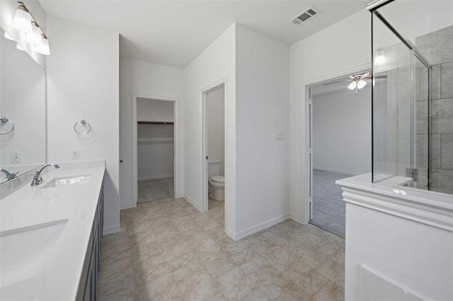 Bathroom featuring tiled shower, double vanity, a walk in closet, and ceiling fan
