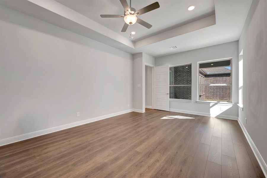 Empty room with ceiling fan, dark wood-style flooring, recessed lighting, and a tray ceiling