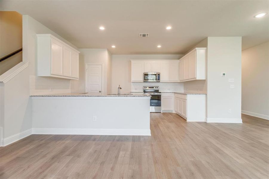 Kitchen featuring tasteful backsplash, white cabinets, stainless steel appliances, light stone countertops, and light wood-type flooring