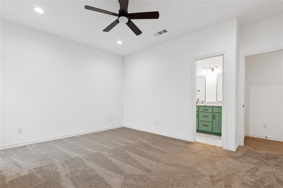 Unfurnished bedroom with ceiling fan, light colored carpet, and ensuite bath