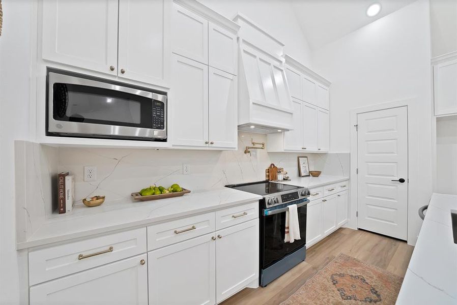Bright kitchen featuring white cabinetry, integrated stainless steel microwave, stone countertops with veining, and wood-finish flooring Bright kitchen featuring white cabinetry, integrated stainless steel microwave, stone countertops with veining, and wood-finish flooring