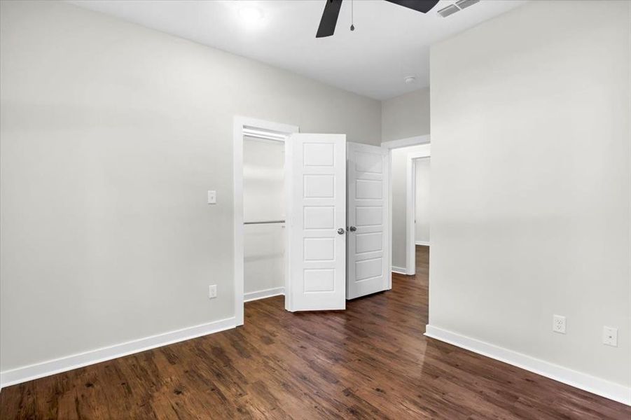Unfurnished bedroom featuring baseboards, dark wood-type flooring, a ceiling fan, and a closet