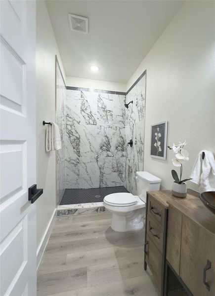 Bathroom featuring tiled shower, hardwood / wood-style flooring, and toilet