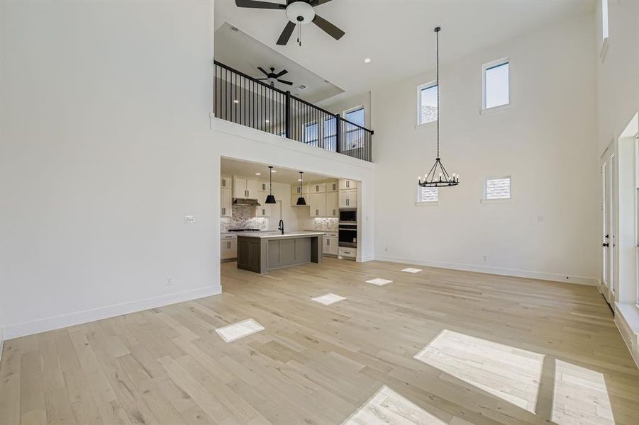 Unfurnished living room featuring light wood finished floors, a ceiling fan, a chandelier, and a towering ceiling Unfurnished living room featuring light wood finished floors, a ceiling fan, a chandelier, and a towering ceiling