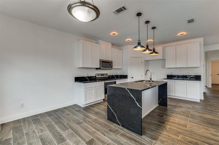 Kitchen featuring decorative light fixtures, white cabinets, stainless steel appliances, a kitchen island with sink, and wood tiled floors Kitchen featuring decorative light fixtures, white cabinets, stainless steel appliances, a kitchen island with sink, and wood tiled floors