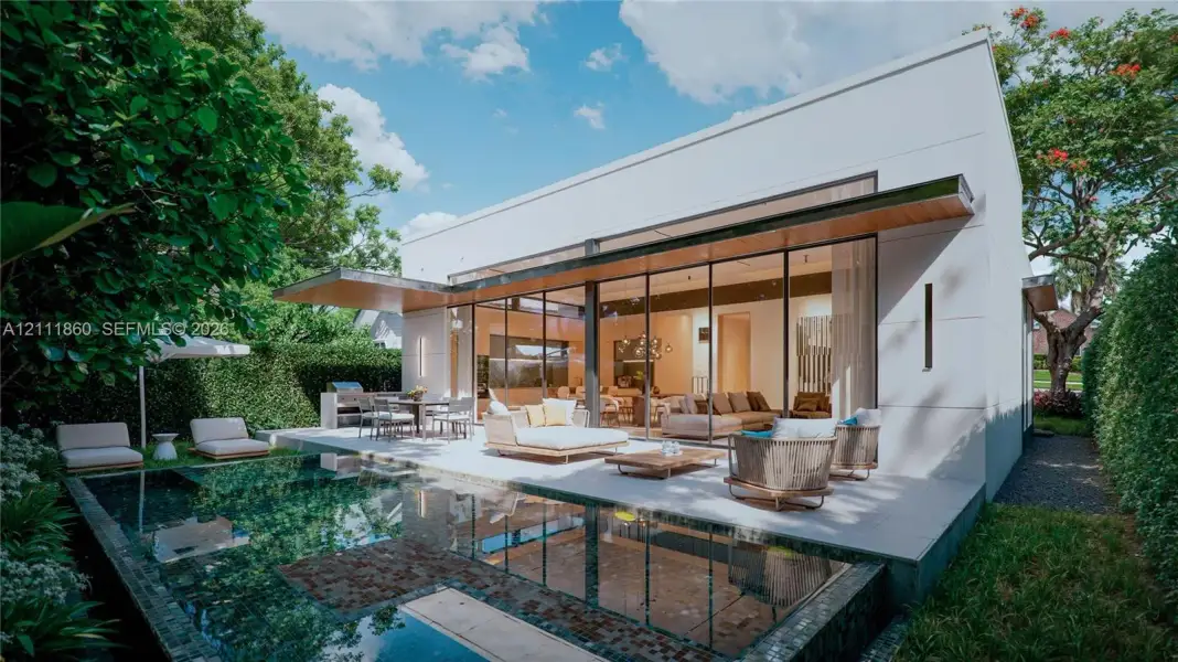 Modern architectural exterior featuring expansive floor-to-ceiling glass panel walls, a covered concrete patio, and a built-in outdoor kitchen with a stone-finish grill station Modern architectural exterior featuring expansive floor-to-ceiling glass panel walls, a covered concrete patio, and a built-in outdoor kitchen with a stone-finish grill station