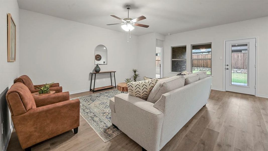 Spacious living area featuring wood-finish flooring, a ceiling fan with integrated lighting, and multiple windows