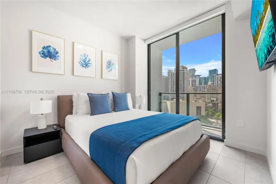 Floor-to-ceiling glass sliding doors, private balcony, neutral large-format tile flooring, and urban cityscape backdrop Floor-to-ceiling glass sliding doors, private balcony, neutral large-format tile flooring, and urban cityscape backdrop