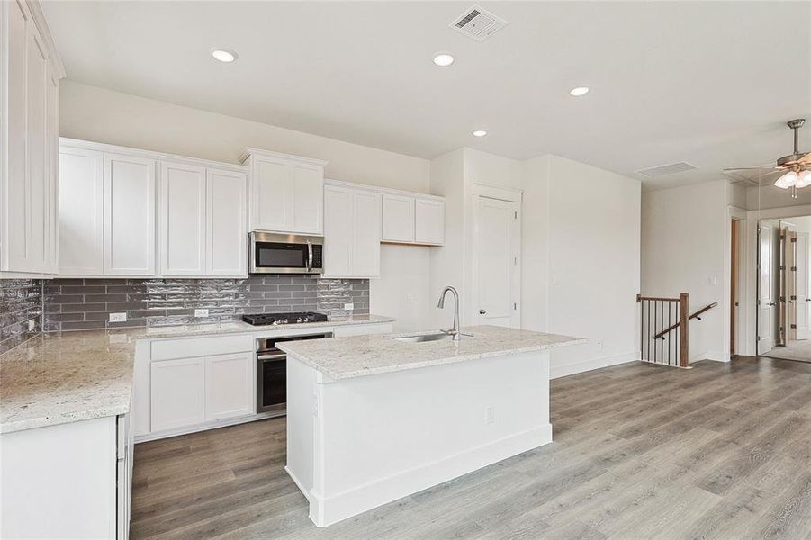 Kitchen featuring ceiling fan, stainless steel appliances, white cabinets, light hardwood / wood-style floors, and a kitchen island with sink