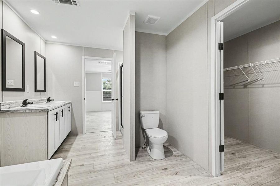 Primary bathroom featuring a dual vanity with two sinks, black hardware, and light-toned wood-look flooring and large walk-in closet