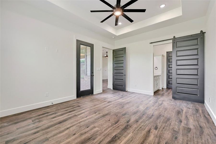 Unfurnished bedroom featuring a raised ceiling, baseboards, a barn door, and wood finished floors