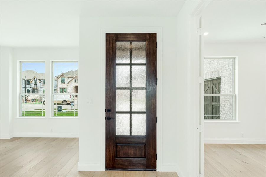 Dark wood interior door with glass panels in white-walled room with light hardwood floors and two windows