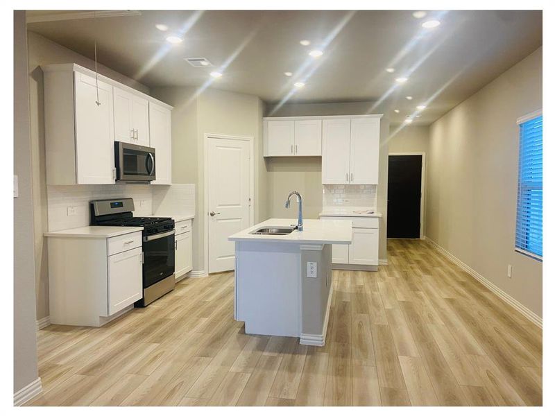 Kitchen featuring white cabinets, sink, appliances with stainless steel finishes, and an island with sink