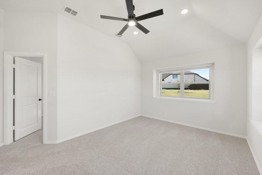 Empty bedroom with vaulted ceiling, black ceiling fan, carpet flooring, and a window with backyard view.