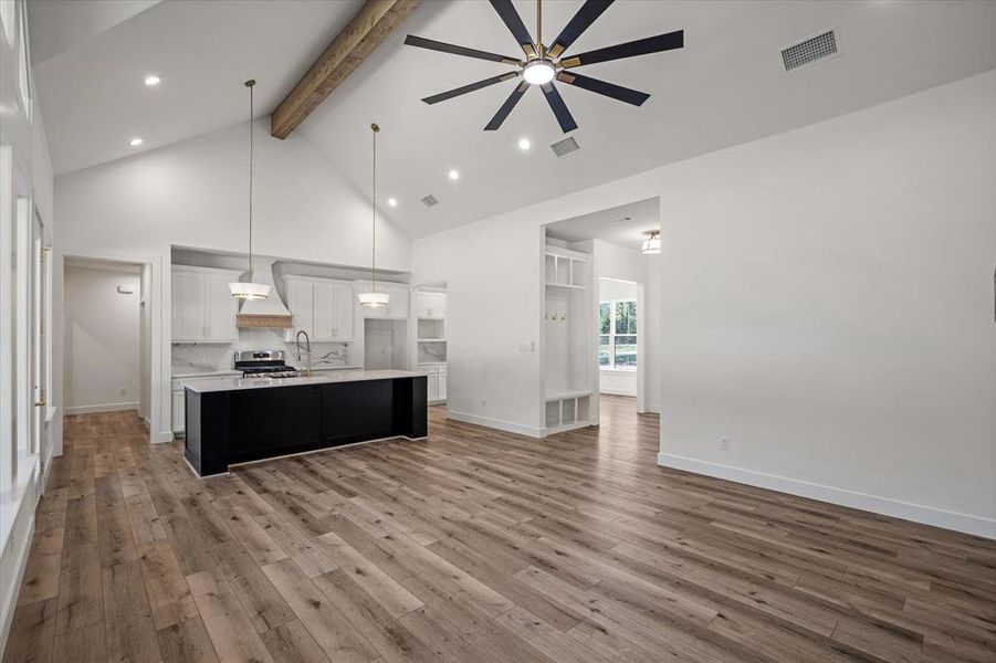 Kitchen featuring dark cabinetry, open floor plan, high vaulted ceiling, a large island with sink, and beamed ceiling