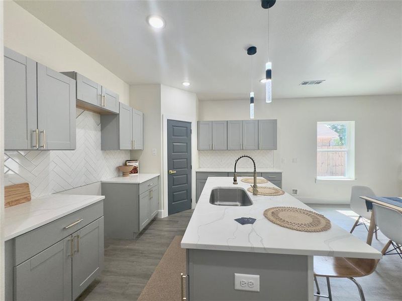 Kitchen with a center island with sink, gray cabinets, tasteful backsplash, and wood-type flooring