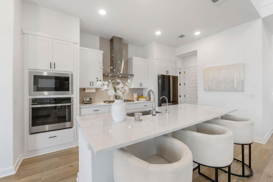 Kitchen featuring light wood-style flooring, wall chimney exhaust hood, appliances with stainless steel finishes, and a sink