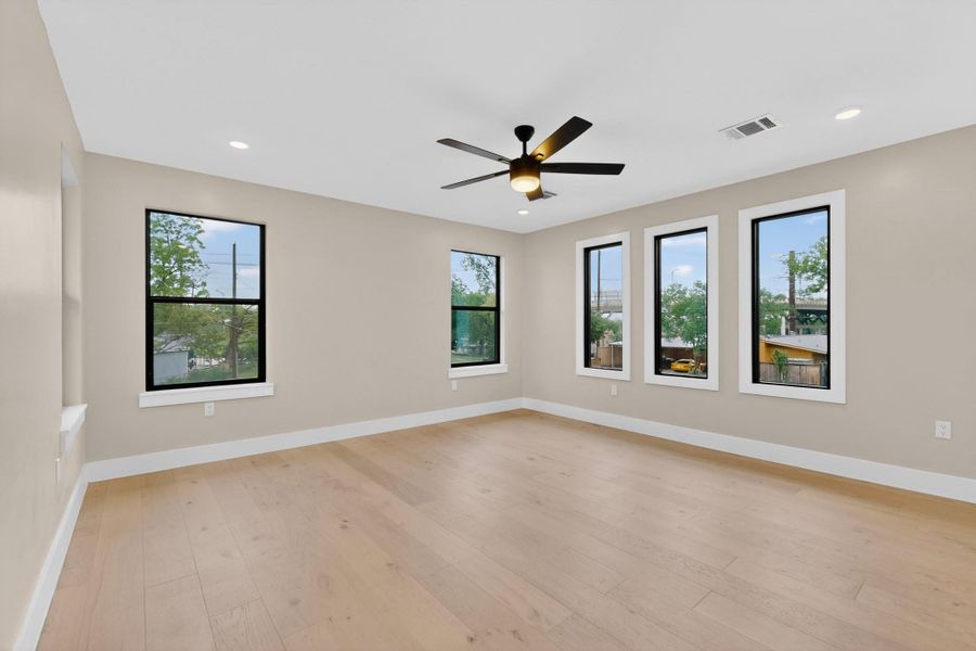 An airy bedroom with light hardwood flooring and multiple windows invites natural illumination.