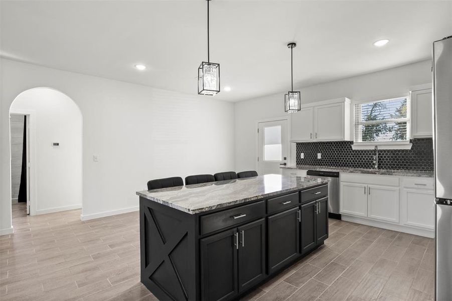 Kitchen with light stone countertops, decorative backsplash, a breakfast bar area, white cabinets, and dark cabinets