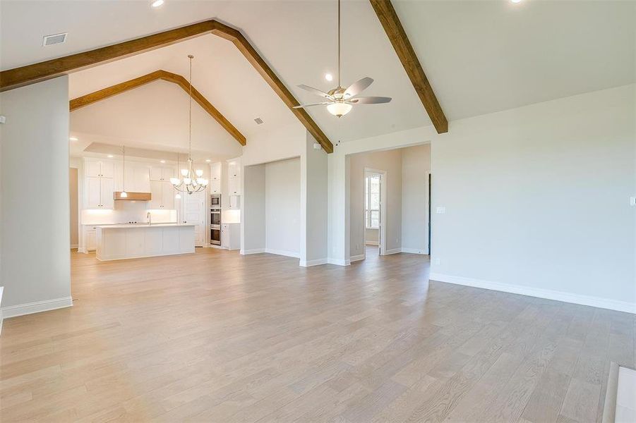 Unfurnished living room with ceiling fan with notable chandelier, beamed ceiling, light hardwood / wood-style flooring, and high vaulted ceiling