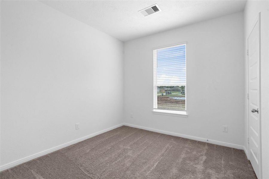 This secondary bedroom offers comfort and style with plush carpet flooring, neutral paint tones, a large window with blinds, and ample sized closet space.