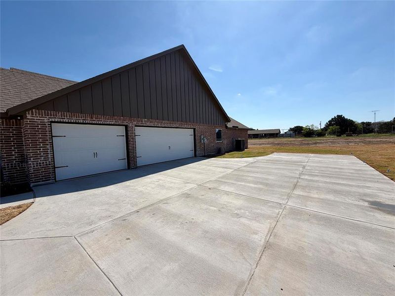 View of side of property featuring driveway, brick siding, board and batten siding, and a garage View of side of property featuring driveway, brick siding, board and batten siding, and a garage