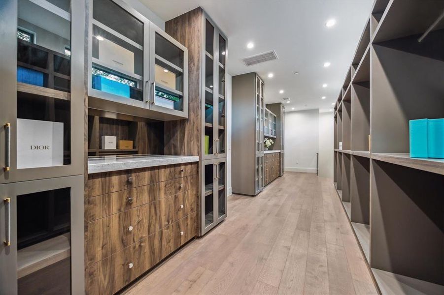 Another view of the well-equipped closet showcases built-in dresser drawers and glass-front display shelving, perfect for organizing all your accessories with style. A back staircase offers convenient access downstairs.