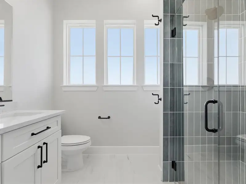 Contemporary bathroom featuring a white vanity with black hardware, a pristine toilet, and a glass-enclosed shower with gray tiled walls