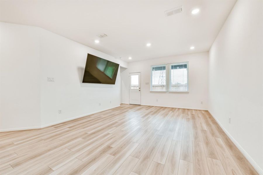 Bright, spacious living area with wood flooring, recessed lighting. Features large windows and a door providing natural light and outdoor access. *The TV will be removed but the wall mount will stay*