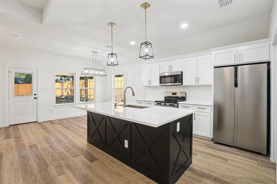 Kitchen featuring stainless steel appliances, white cabinets, a kitchen island with sink, dark cabinets, and recessed lighting Kitchen featuring stainless steel appliances, white cabinets, a kitchen island with sink, dark cabinets, and recessed lighting