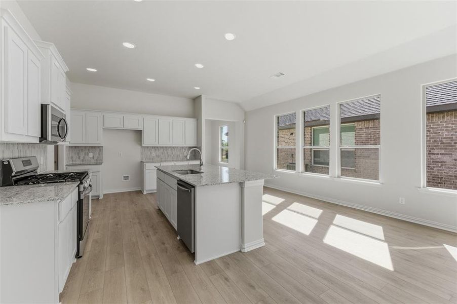 Kitchen featuring stainless steel appliances, white cabinetry, light stone countertops, a center island with sink, and recessed lighting