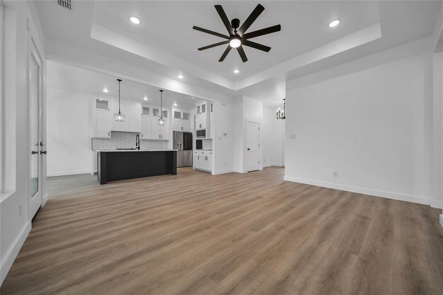 Unfurnished living room featuring a raised ceiling, ceiling fan, sink, and dark hardwood / wood-style floors