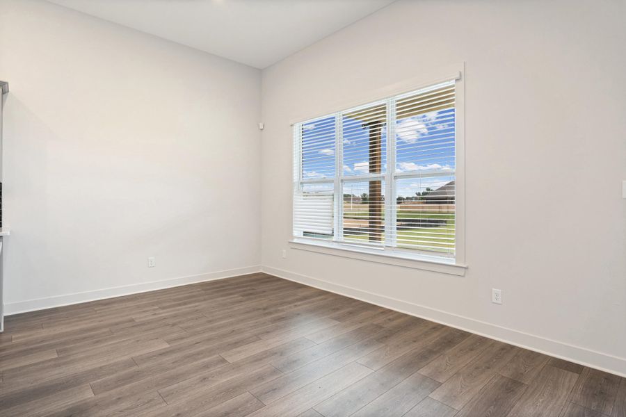 Spacious room featuring wood-finish flooring, white baseboards, and a large window with white blinds Spacious room featuring wood-finish flooring, white baseboards, and a large window with white blinds