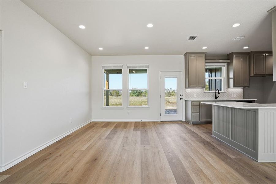 Kitchen featuring light wood-type flooring, tasteful backsplash, gray cabinets, recessed lighting, and light stone countertops Kitchen featuring light wood-type flooring, tasteful backsplash, gray cabinets, recessed lighting, and light stone countertops