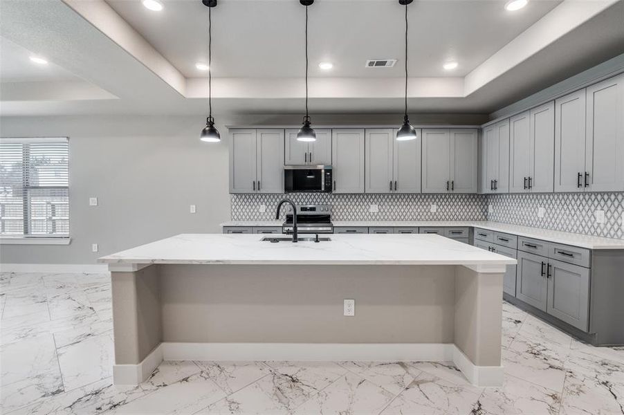 Kitchen featuring gray cabinetry, a raised ceiling, a breakfast bar, and recessed lighting