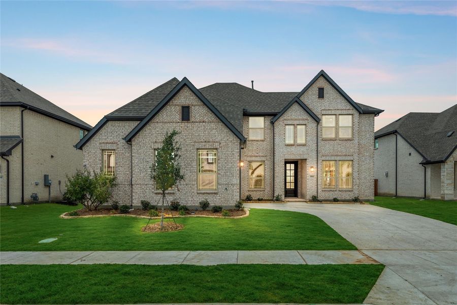 Two-story brick home with dark roof, large windows, and manicured front lawn with concrete driveway