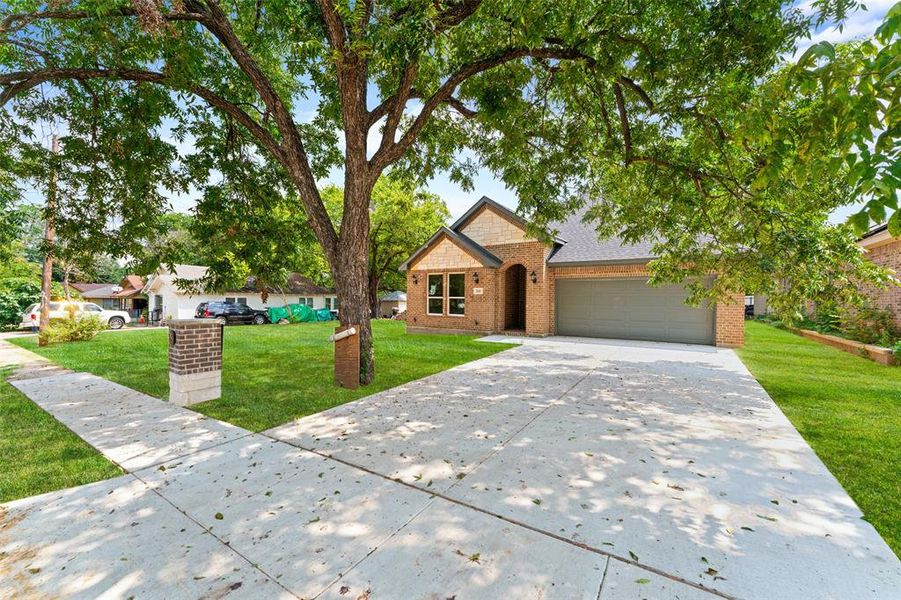 View of front of house with an attached garage, driveway, brick siding, a front lawn, and a shingled roof