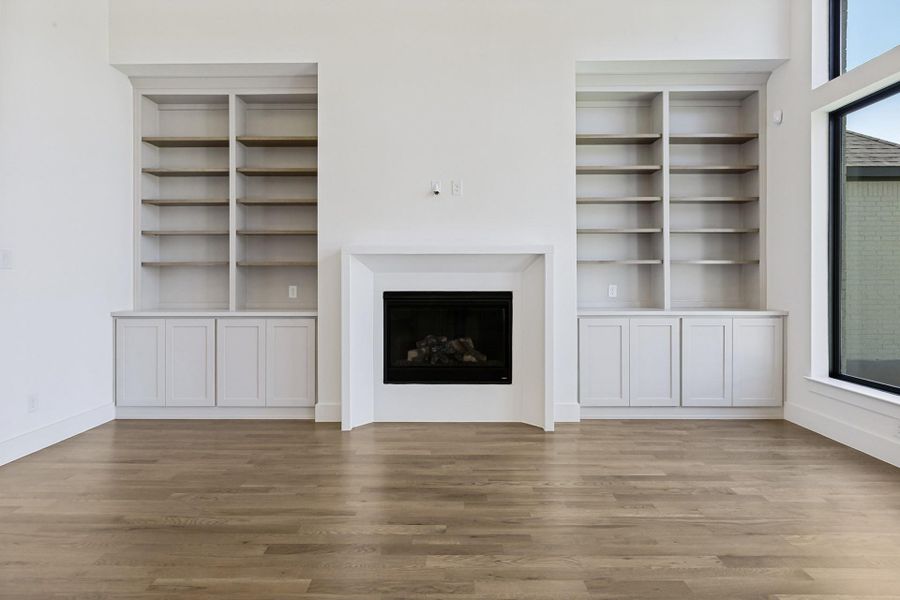 Polished wood floors anchor a minimalist fireplace flanked by custom built-in shelving and cabinetry.