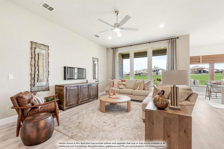 Living room with ceiling fan, large windows, neutral sofa, leather chair, and wood media console on light hardwood floors