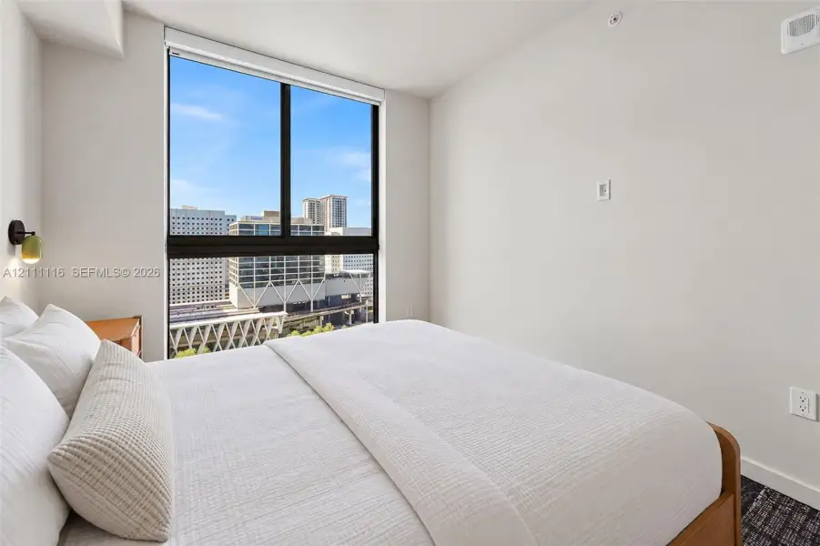 Floor-to-ceiling window featuring city scenery, wall-mounted modern sconce, and textured dark carpeting