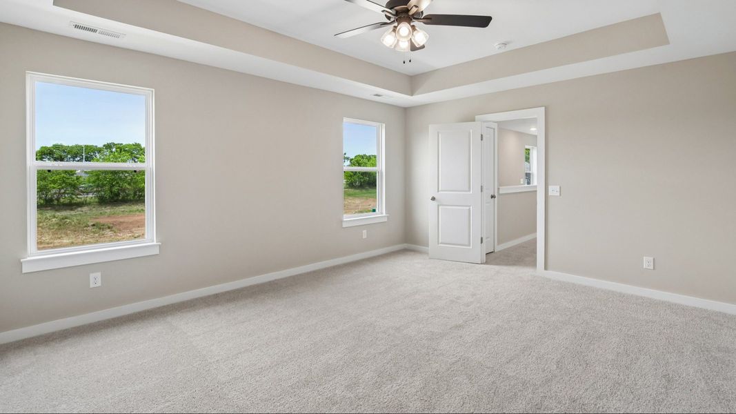Bedroom with tray ceiling, windows, and entrance to primary bedroom