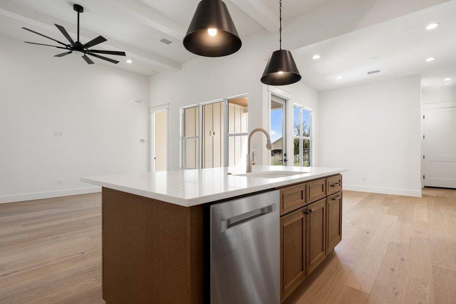Kitchen area featuring an island with a light-colored countertop, a sink with a gooseneck faucet, a stainless steel dishwasher, and wooden cabinetry