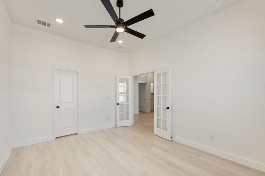 Empty bedroom with light wood floors, black ceiling fan, and white French doors Empty bedroom with light wood floors, black ceiling fan, and white French doors